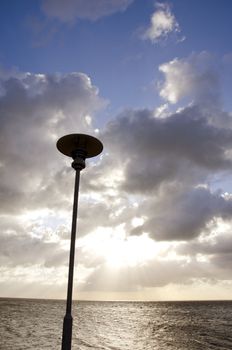 park lamp on background of cloudy sky and sunlight penetrating through clouds.
