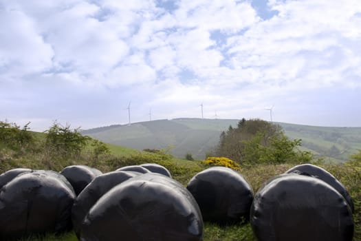 windmill on lush irish countryside landscape in glenough county tipperary ireland with plastic wrapped bales in foreground