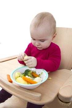 young child in red shirt eating vegetables in wooden chair.