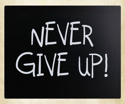 "Never give up" handwritten with white chalk on a blackboard