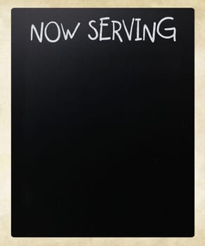 "Now serving" handwritten with white chalk on a blackboard