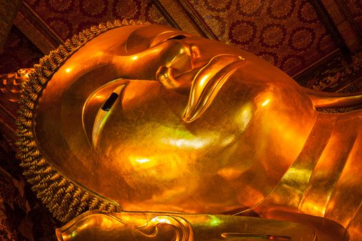 Reclining Buddha gold statue face close up. Wat Pho, Bangkok, Thailand