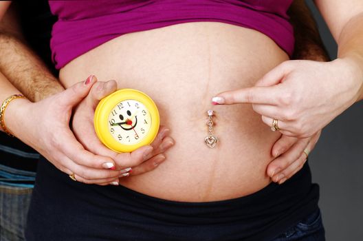Funny pregnancy concept with mother to be showing the clock to her belly, implying that it is time to give birth.