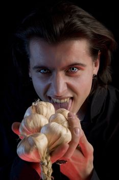 Vampire with scary eyes is licking garlic, red horror light, isolated on black background 