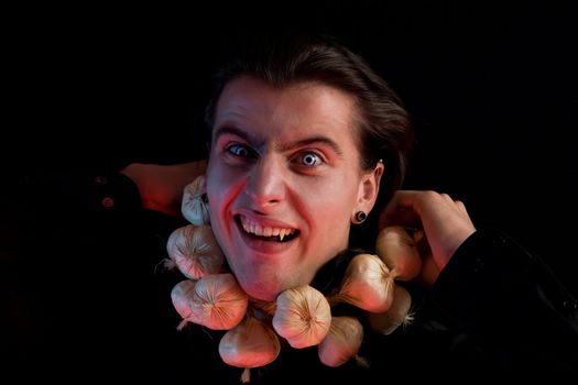 Funny vampire with scary eyes suffocated from being choked by garlic, isolated on black background 