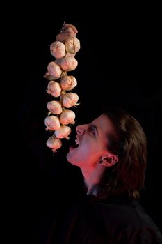 Humorous shot of vampire eating garlic, red horror light, isolated on black background 