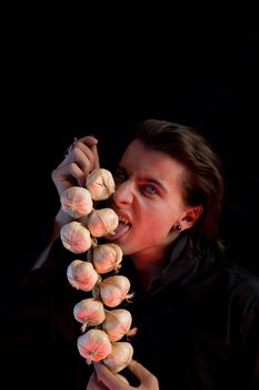 Evil vampire with scary eyes is licking garlic, red horror light, isolated on black background 