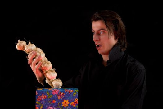 Shocked vampire with gift box taking out garlic, isolated on black background 