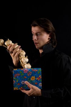 Funny shot of amazed vampire with gift box taking out garlic, isolated on black background 