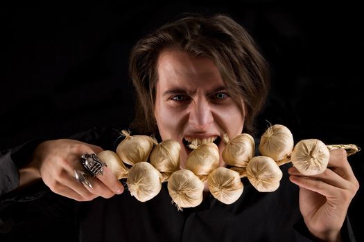 Evil vampire with scary eyes eating garlic, isolated on black background 