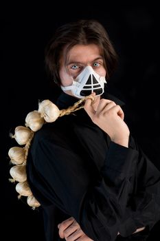 Humorous shot of vampire in respirator holding garlic, isolated on black background 