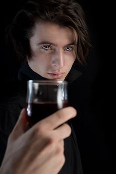 Handsome vampire with pale skin and blue eyes holding glass of wine or blood, Halloween theme 