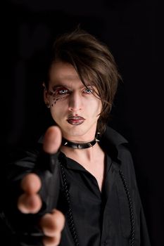 Gothic boy with artistic make-up pointing his hand as a gun, isolated on black background 