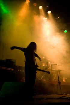 Unrecognizable musician with guitar on the stage, laser show and smoke 