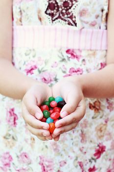 Little girl offering a handful of jellybeans. Extreme shallow depth of field with selective focus on little girls fingers and jellybeans in foreground.
