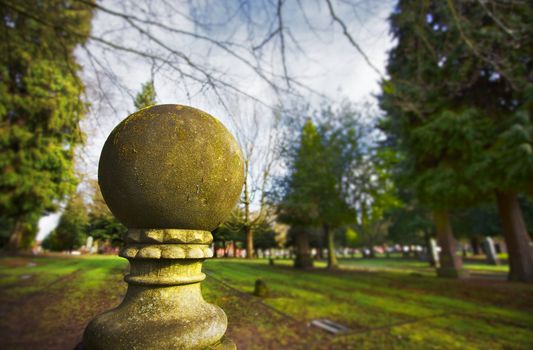 Old weatherd moss covered stone ball sculture with a background of a lawn and trees