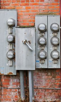 Eight old weathered rusty power meters on a orange and red brick wall