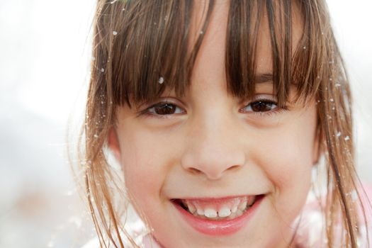 Closeup portrait of a smiling happy little girl with snow flakes in her hair