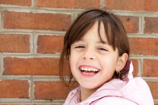 Laughing little girl in winter jacket in front of a brick wall