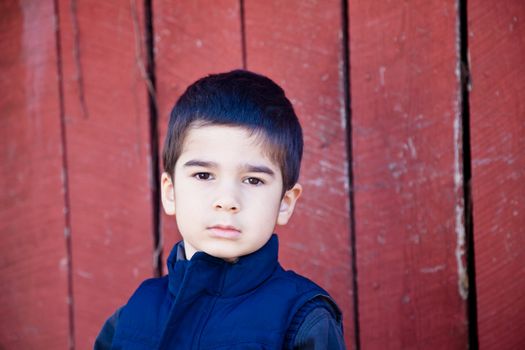 Serious Little Boy Making Eye Contact in front of red textured background with a sad and thoughtfull expression.