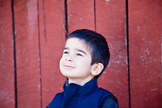 Little boy looking up and to the left in front of red textured background with a joyfull day dreaming expression.