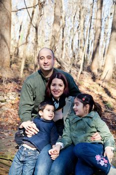 Portrait of a happy smiling family in the forest. Mother and father are looking at the camera and the boy and girl are making eye contact looking at each other.