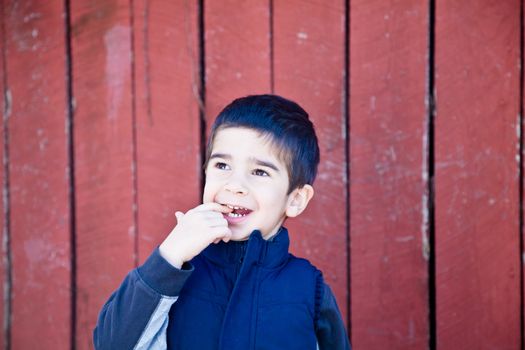 Little boy looking up and to the left in front of red textured background biting on his finger with an amazed expression.