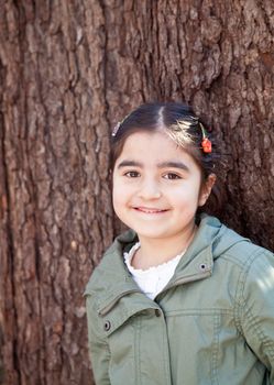 Portrait of a smiling happy little girl in front of a tree with bark texture in the background