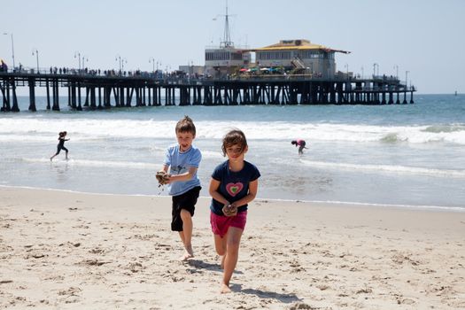 Little girl and boy running on the beach and playing with wet sand.