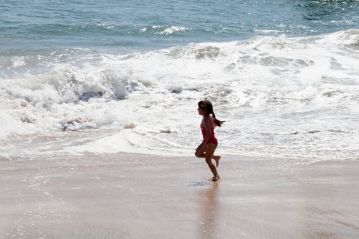 Little girl running and exercising on the beach in the breaking waves.