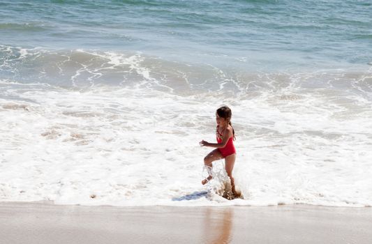 Little girl running and exercising on the beach in the breaking waves.