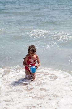 Very excited little girl running in the ocean surf with a blue bucket