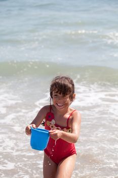 Very excited little girl running in the ocean surf with a blue bucket