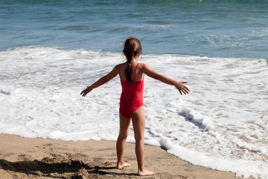 Little girl playing in the surf on the beach by the ocean waiting for the foamy water to reach her feet.