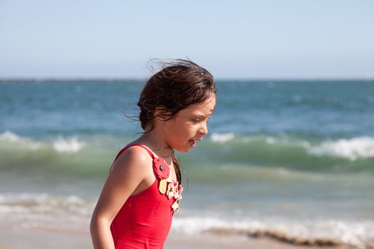 Little girl walking and talking on the beach with the ocean and waves in the background.