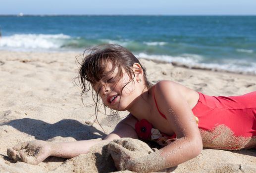 Little girl hanging out on the beach covered in sand. She is relaxed with her eyes closed.