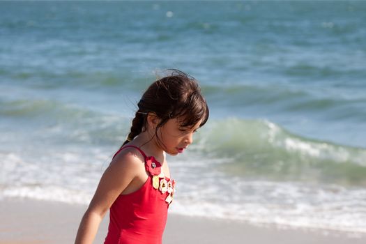 Little girl lost in thought walking on the beach by the ocean.