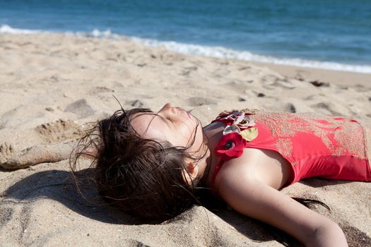 Little girl hanging out on the beach covered in sand. Closeup of a sleeping girl on the beach with ocean in the background
