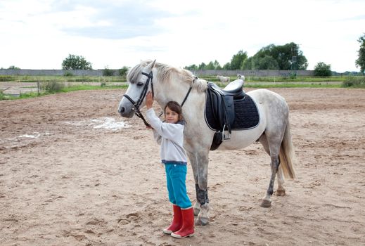 Little girl petting and standing next to her horse ready for a horseback riding lesson.