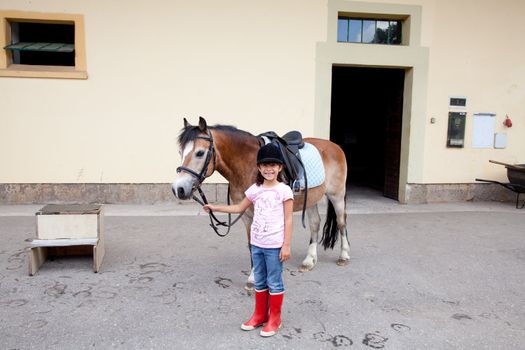 Little girl standing next to her horse ready for a horseback riding lesson.