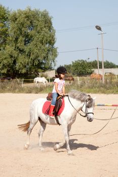 Little girl riding a horse and taking horse back riding lessons outdoors.