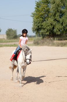 Little girl riding a horse and taking horse back riding lessons outdoors.