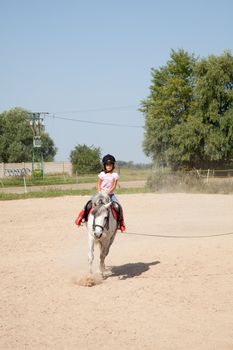 Little girl riding a horse and taking horse back riding lessons outdoors.