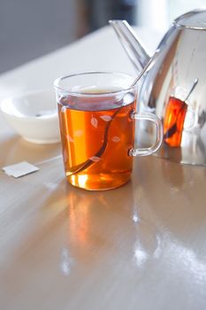 Daily break with glass mug with tea, teapot en teabag on table - vertical image