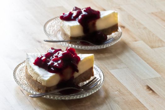 Wooden table with two pieces Mon Chou tart decorated with cherry sauce on glass saucers - horizontal image