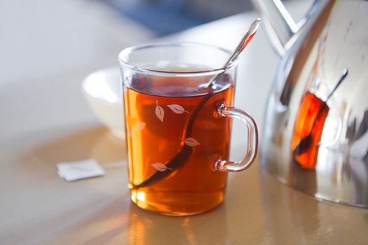 Daily break with glass mug with tea, teapot en teabag on table - horizontal image