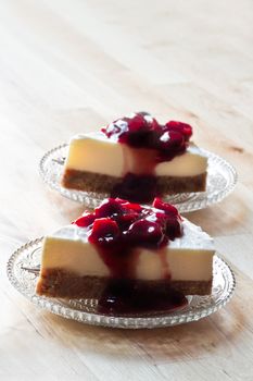 Wooden table with two pieces Mon Chou tart decorated with cherry sauce on glass saucers - vertical image