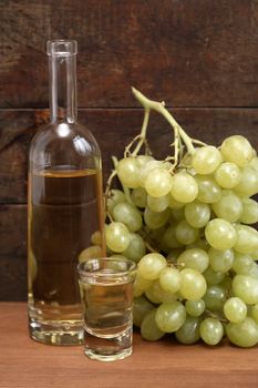 Open bottle of grappa near wineglass and bunch of grapes against old wooden background