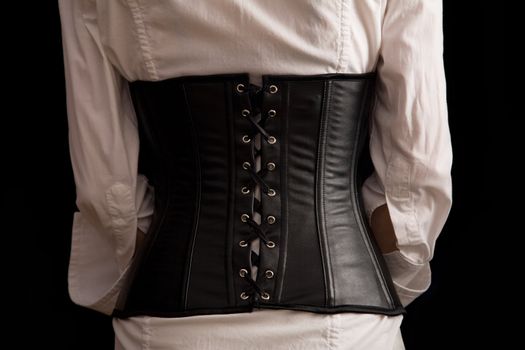 Rear view of girl in leather corset, isolated on black background  