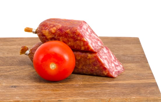 cut smoked sausage pieces and tomato on cutting board isolated on white background.